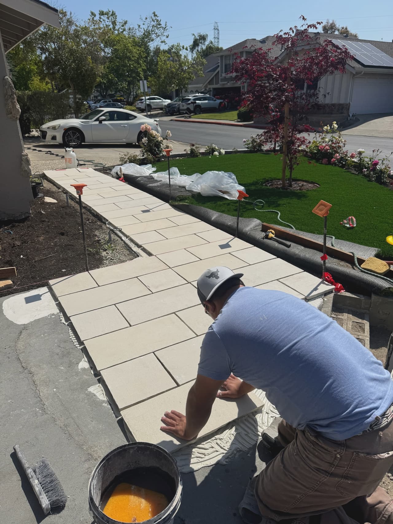 A crew member kneeling to work the joints of a newly laid stone walk beside a lawn.