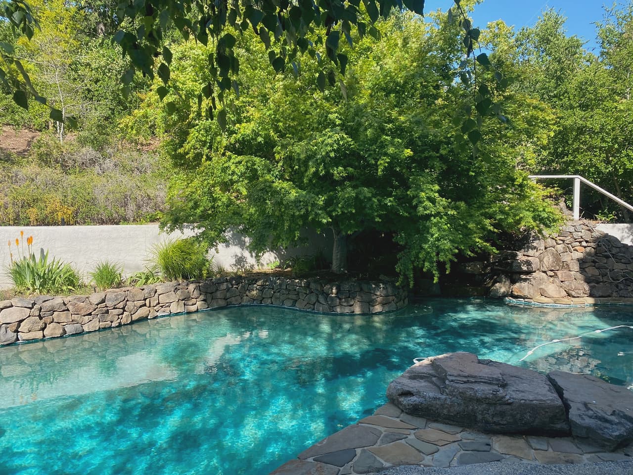 A free-form pool edged in natural boulders and flagstone below a dry-stone bank.