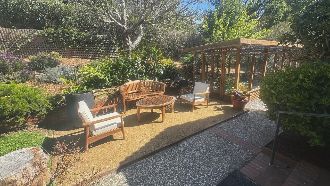 A completed decomposed granite terrace furnished with teak seating, edged by planting and a low wall.