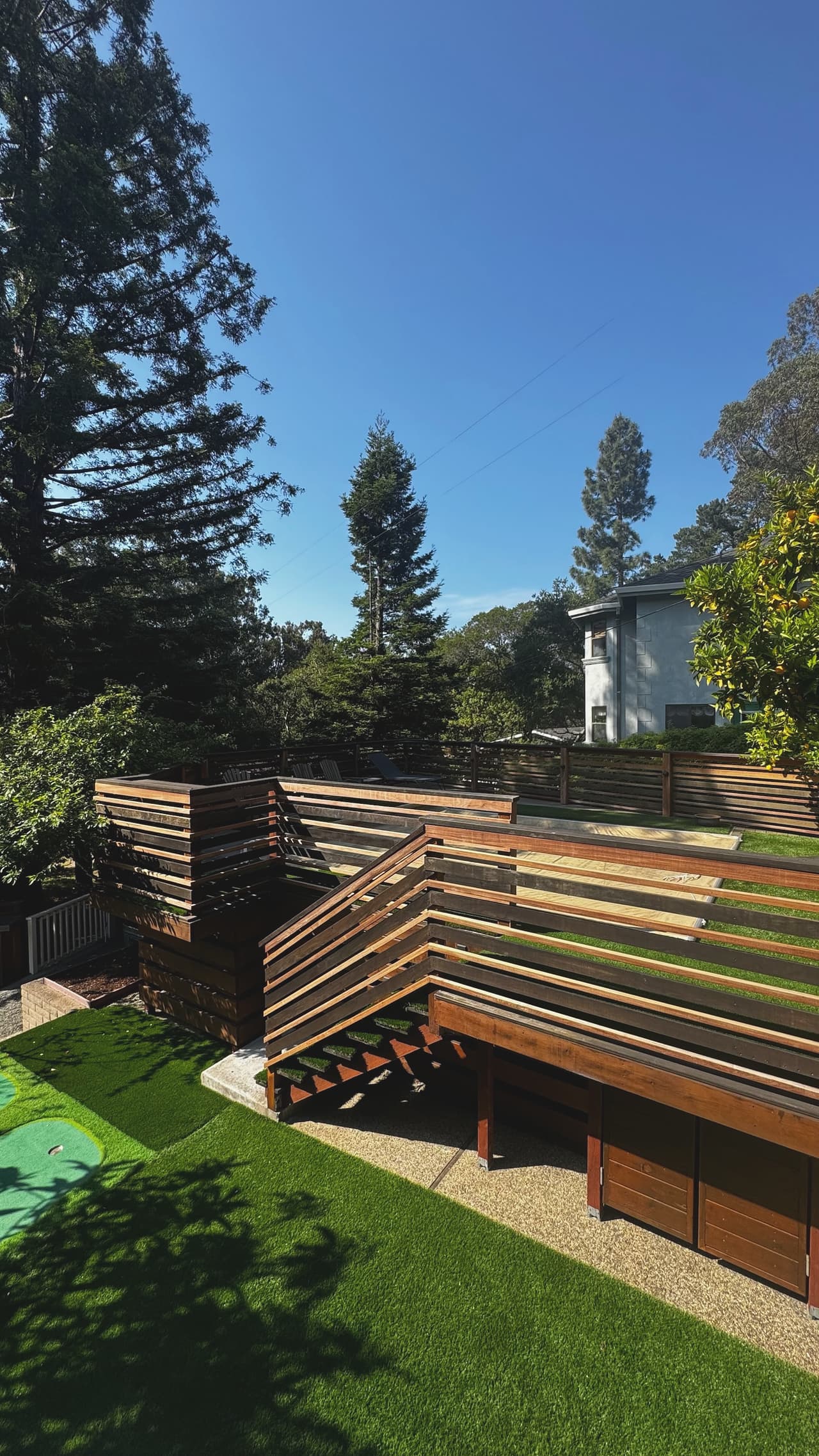 A finished multi-level structure of stacked horizontal redwood slats stepping down a slope to a lawn.